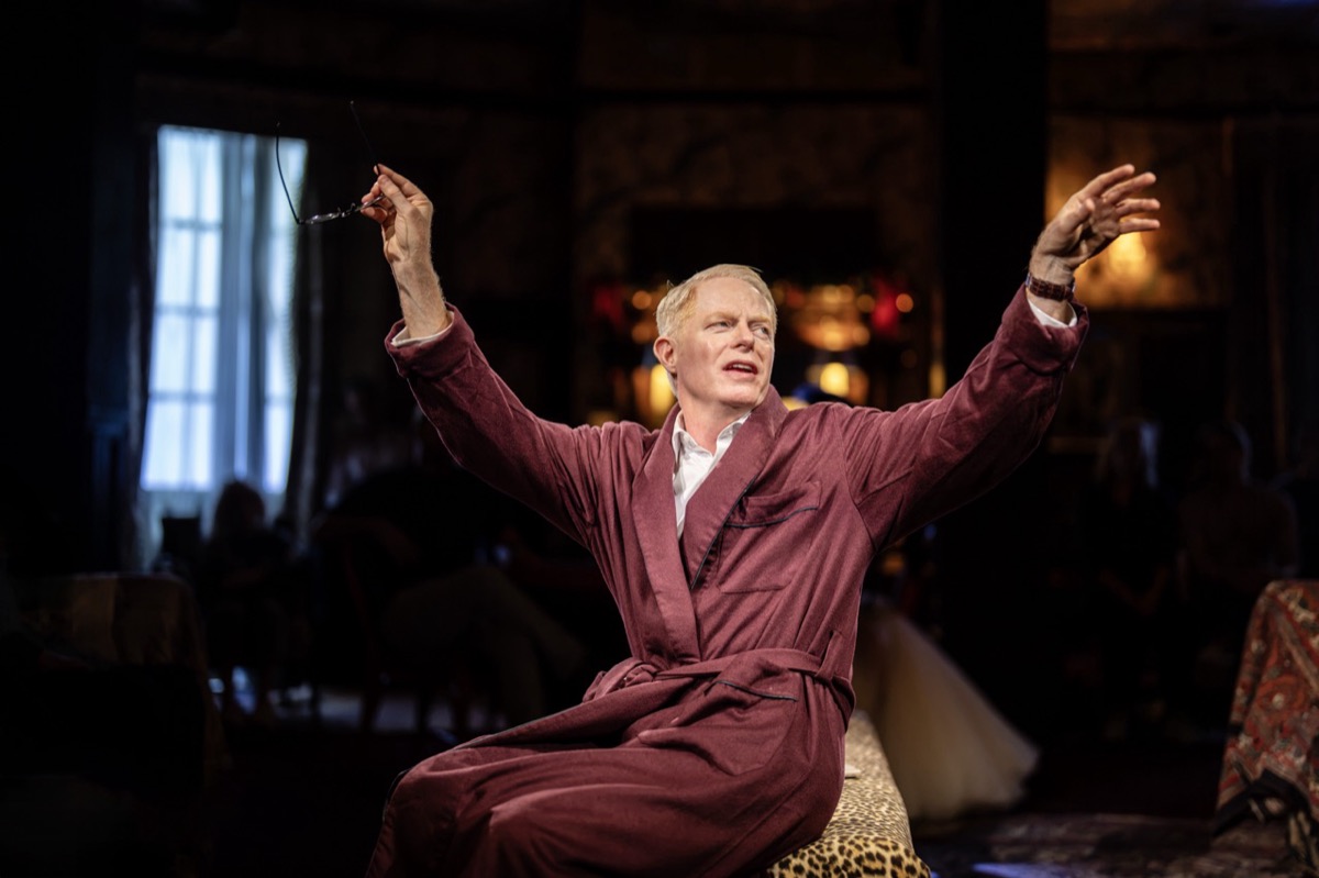 Jesse Tyler Ferguson on stage in a burgundy dressing gown, arms raised