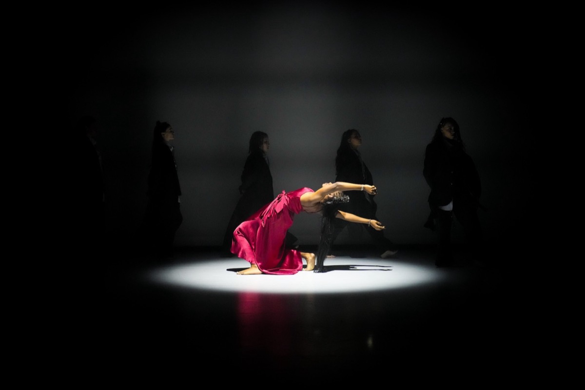An AMDA dancer in a red dress arching back in a pool of spotlight